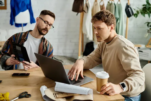 Due uomini, una coppia gay, si siedono a un tavolo a lavorare insieme su un portatile in un laboratorio di design. — Foto stock