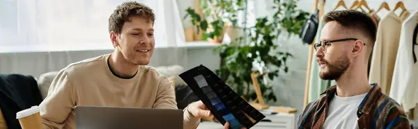 Two men sit by each other, focused on a laptop, working on creating trendy attire together. — Stock Photo