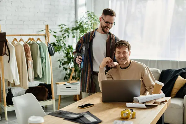 Dois homens, casal gay colaborar em um laptop em uma oficina de designer criando trajes na moda. — Fotografia de Stock