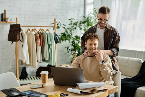 Un hombre se sienta frente a una computadora portátil, diseñando atuendos de moda en un taller de diseño. — Stock Photo