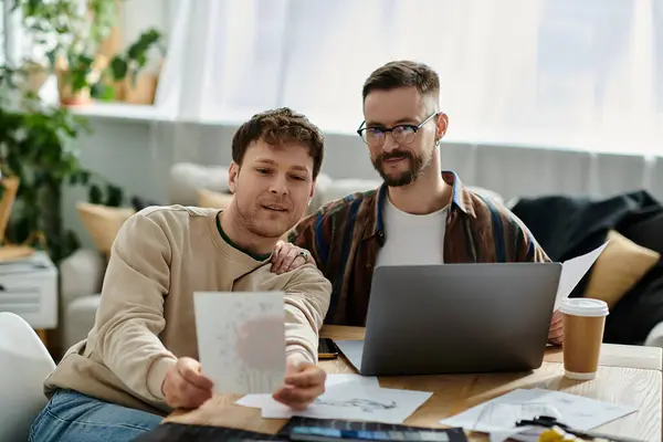 Two men, a gay couple, sit at a table, engrossed in their work on a laptop in a designer workshop. — Stock Photo