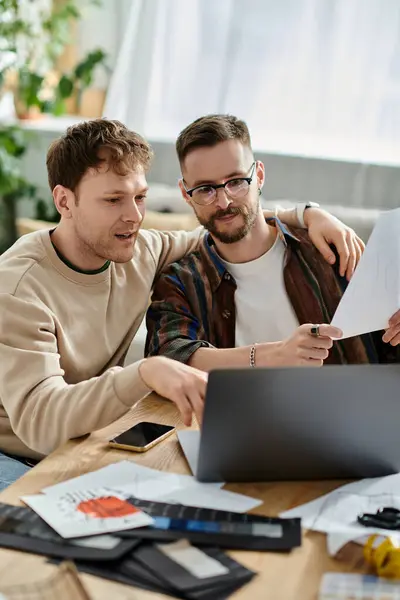 Two men, a gay couple, sit at a table, intensely focused on a laptop while working together in a designer workshop. — Stock Photo