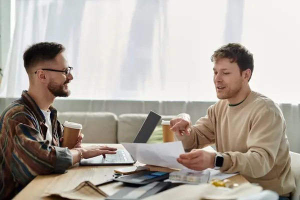 Una coppia gay innamorata progetta insieme abiti alla moda a un tavolo da workshop. — Foto stock