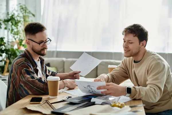 Two men in love collaborate on designing trendy attire in a designer workshop, surrounded by papers. — Stock Photo