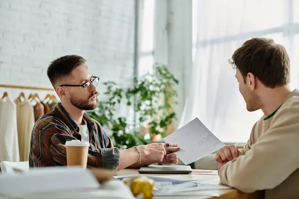 Dos hombres colaboran en el diseño de atuendos de moda en un taller. — Stock Photo