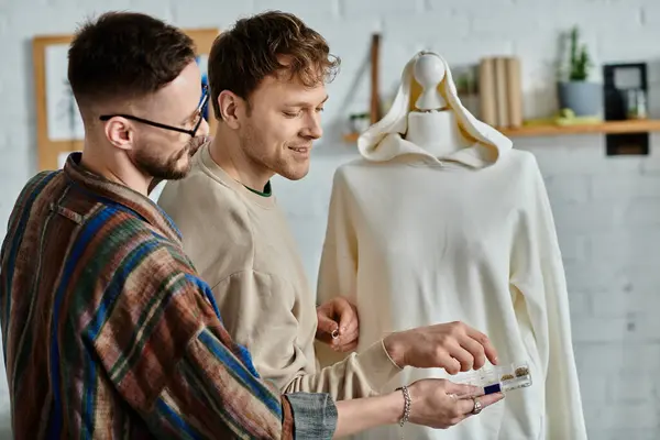 Two men, a gay couple in love, carefully examine a chic dress on a mannequin in their designer workshop. — Stock Photo