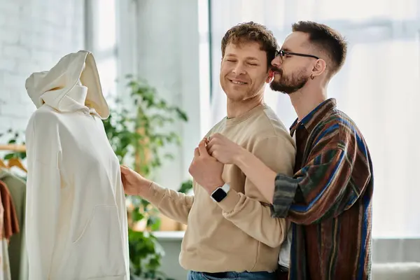 A gay couple stands together in a designer workshop, collaborating on creating trendy attire. — Stock Photo