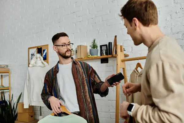 Two men, a gay couple, standing side by side in a designer workshop, working together on trendy attire. — Stock Photo