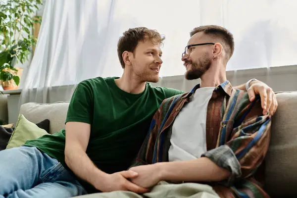 Two trendy men, part of a gay couple, sit comfortably on the back of a couch in a stylish workshop. — Stock Photo