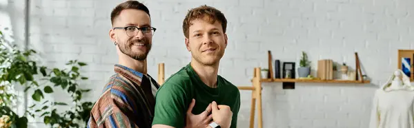 Deux hommes, un couple gay, se tiennent côte à côte dans un atelier de designers, collaborant sur leurs créations vestimentaires branchées. — Photo de stock