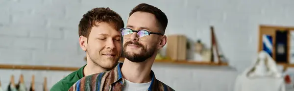 Dos hombres, una pareja gay, se paran uno al lado del otro en un taller de diseño, elaborando apasionadamente atuendos de moda. - foto de stock