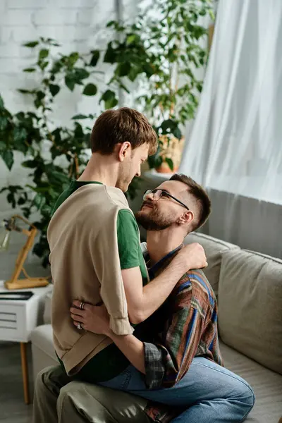 Two men, part of a gay couple, sit on top of a stylish couch in a designer workshop, hugging with love — Stock Photo