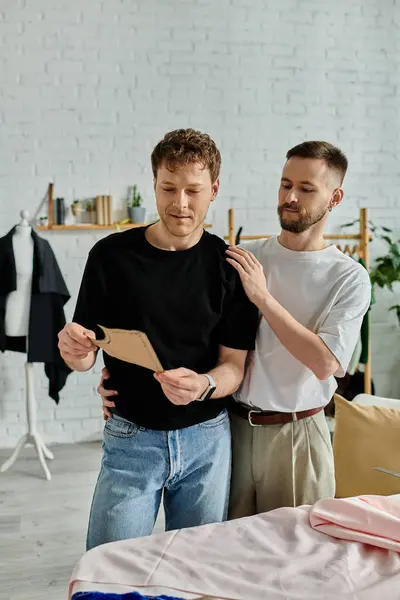Dois homens, um casal gay, estão juntos em uma oficina de designer, colaborando em trajes da moda. — Fotografia de Stock