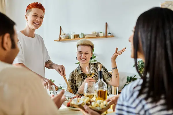 Un grupo diverso de personas, incluyendo una pareja lesbiana cariñosa, comparten una comida y una conversación alrededor de una mesa. - foto de stock