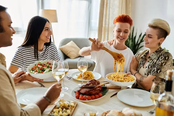 Un grupo multicultural disfrutando de una comida en una mesa, incluyendo una pareja lesbiana cariñosa. - foto de stock