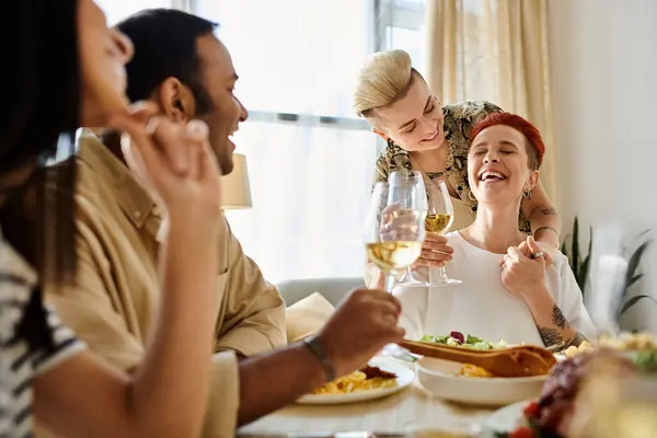 A diverse group of friends sharing a meal around a table, including a loving lesbian couple. — Stock Photo