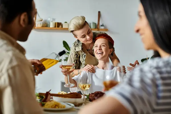 A loving lesbian couple shares a meal with diverse friends around a table at home. — Stock Photo