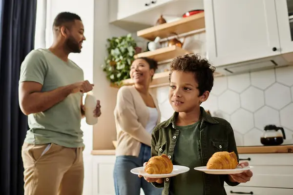 Un hombre y una mujer se paran en una cocina mientras un niño sostiene un plato de comida. — Stock Photo