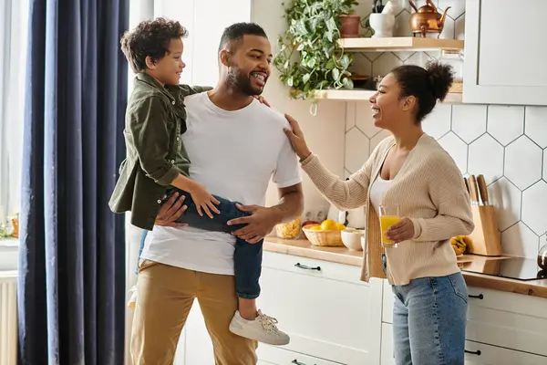 Man holding child, woman beside him in kitchen. — Stock Photo