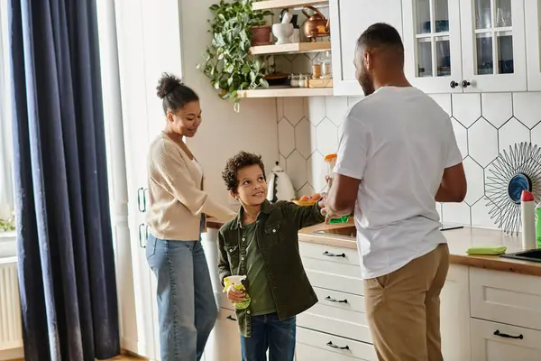 An African American man and woman clean with a child in a cozy kitchen. — Stock Photo