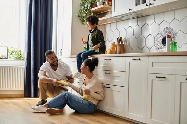 A man and a woman sit on the kitchen floor, enjoying each others company, with son. — Stock Photo