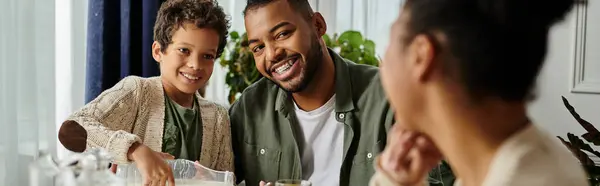 An African American man and boy sit at a table, engaged in conversation and sharing a moment together, with woman. — Stock Photo