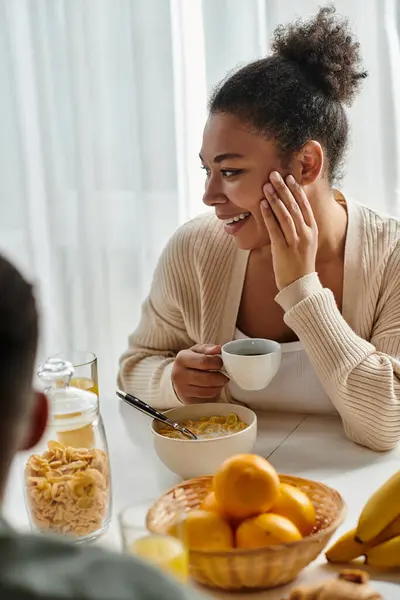 Woman of African descent happily sitting at a table enjoying a bowl of cereal. — Stock Photo