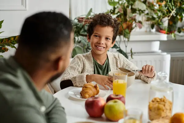 Un hombre y un niño se sientan en una mesa, disfrutando de una comida juntos. - foto de stock