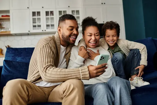 An African American family engrossed in a smartphone on a cozy couch. — Stock Photo