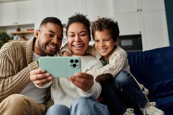 Man, woman, and child engrossed in phone on couch. — Stock Photo