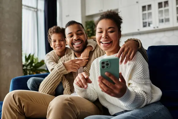 A man and a woman sitting on a couch, focused on a cell phone screen, with son. — Stock Photo