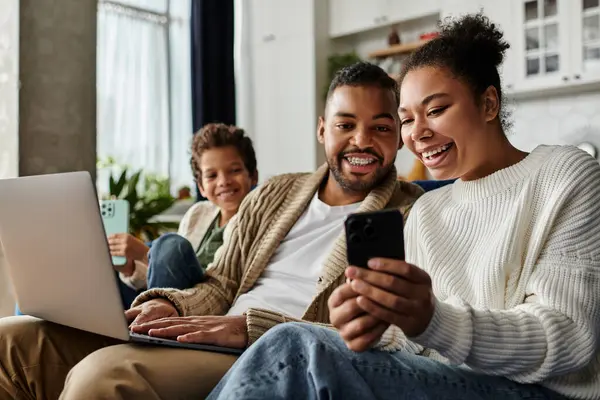 Man and woman engrossed in cell phone while seated on couch, with son. — Stock Photo