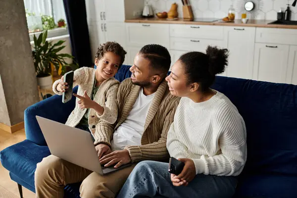 La familia afroamericana se relaja en un sofá, absorta en una pantalla de computadora portátil. — Stock Photo