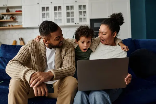 Un uomo e una donna sono seduti su un divano con un bambino, tutti guardando un computer portatile. — Foto stock