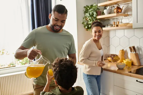 El hombre vierte jugo de naranja para su hijo en la cocina. - foto de stock