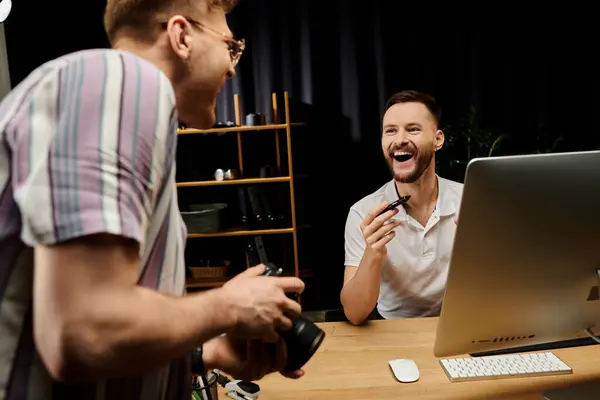 Dos hombres, uno riéndose, trabajan juntos frente a una computadora. - foto de stock