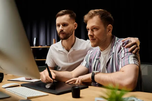 Two men working on a computer at a desk. — Stock Photo