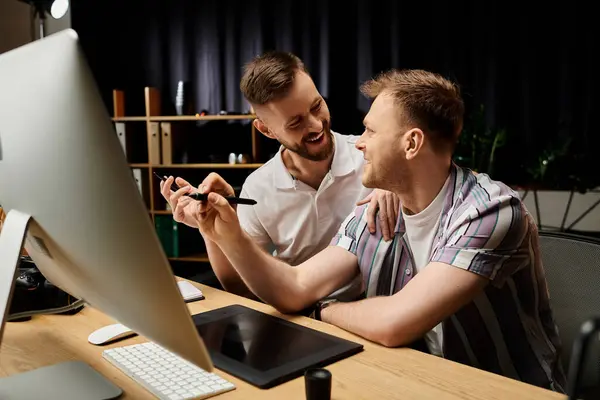 Two men in casual attire work together at a desk, focused on a computer screen. — Stock Photo
