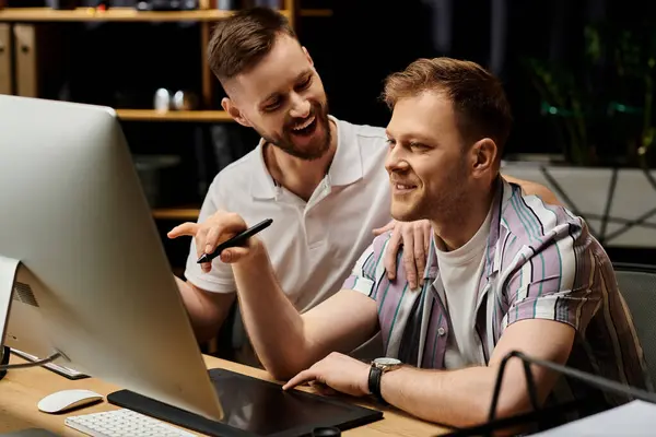 Dos hombres felices y elegantes trabajando juntos en una oficina moderna, enfocados en una pantalla de computadora. - foto de stock