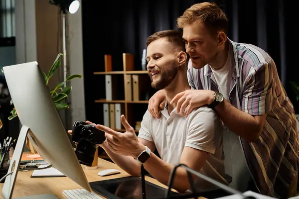 Two men engage with a computer screen in a modern office setting. — Stock Photo