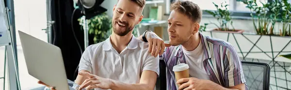 Two men in colorful clothes working and discussing on a laptop at a table. — Stock Photo