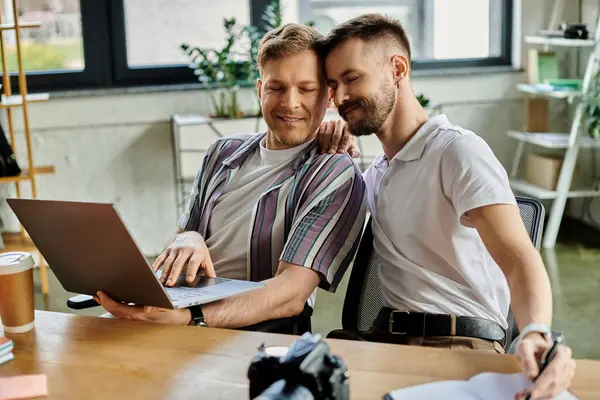 Two men in casual attire sitting at table, engrossed in work on laptop. — Stock Photo