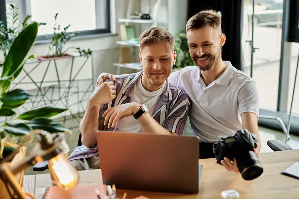 Two men in casual clothing sitting at a table, engrossed in using a laptop. — Stock Photo