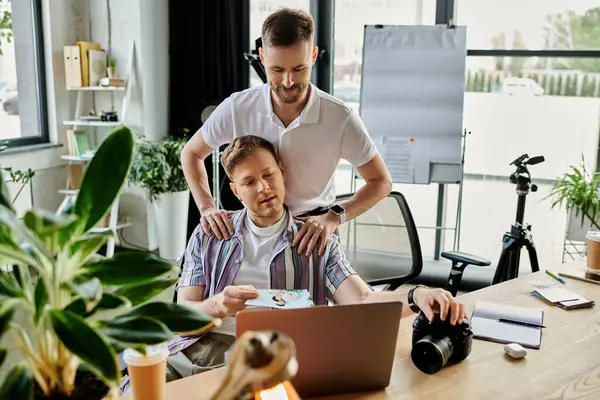 Ein Mann, der sich in einem gemütlichen Arbeitsraum neben seinem schwulen Partner auf seinen Laptop konzentriert. — Stockfoto