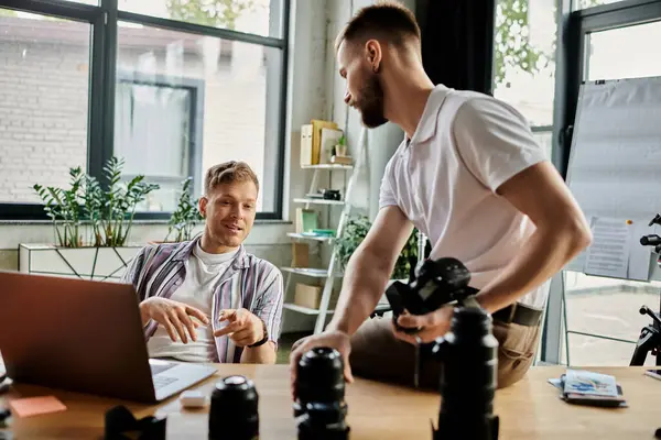 Two men wearing comfy attires sitting at a table, working on a laptop together. — Stock Photo