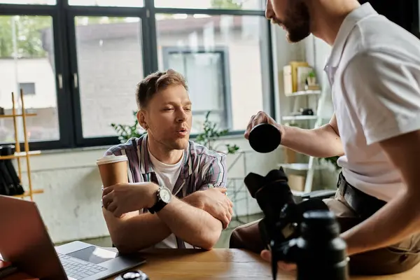 Two men in casual attire sitting at a table, one holding a camera, collaborating on a project. — Stock Photo