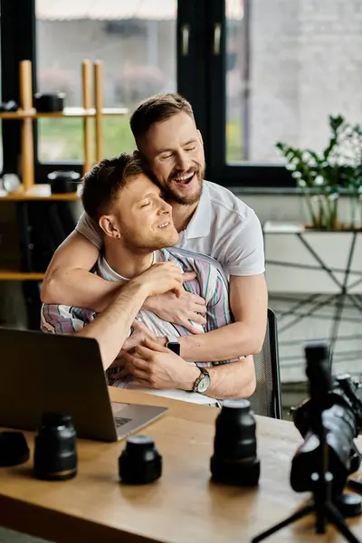 Two men in casual attire sharing a warm embrace while working in front of a laptop. — Stock Photo