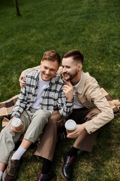 Two men in casual attire enjoy a peaceful moment on a blanket in the grass. — Stock Photo