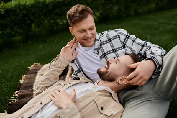 Two men in comfy attire laying on a blanket in green grass enjoying each others company. — Stock Photo