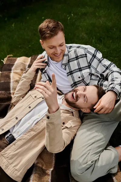 Dos hombres se relajan encima de una manta en un entorno tranquilo al aire libre. - foto de stock